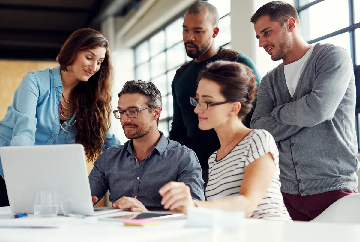 Small business team gathered around a laptop in a bright, open office