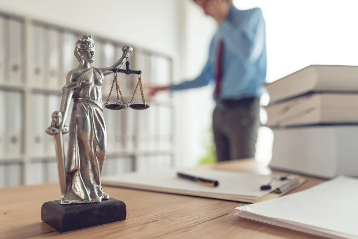 Lady Justice statue on a law office desk, with an attorney on a phone call in the background