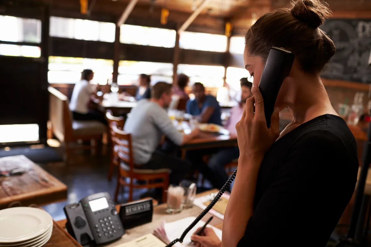 Restaurant staff member on a phone call at the host stand while guests dine in the background